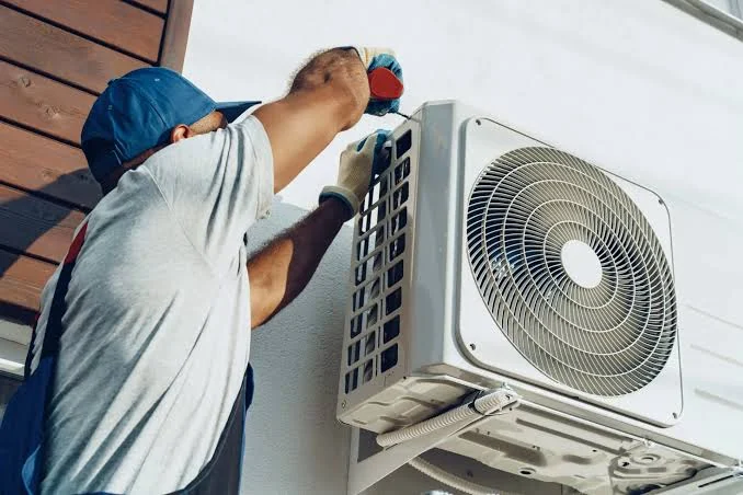 Technician securing an outdoor air-conditioning unit to an exterior wall