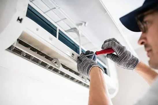 Technician repairing a wall-mounted air conditioner with a hand tool